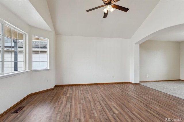 empty room featuring lofted ceiling, wood finished floors, arched walkways, and ceiling fan