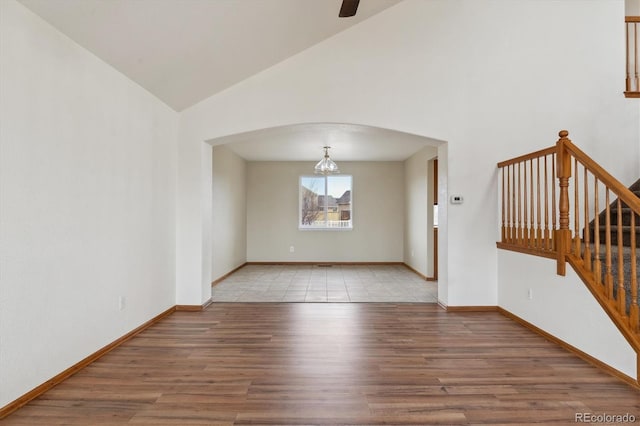 empty room featuring high vaulted ceiling, baseboards, arched walkways, light wood-style floors, and a ceiling fan