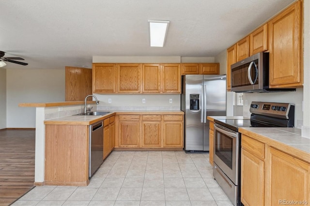 kitchen with a sink, light tile patterned floors, appliances with stainless steel finishes, and a peninsula