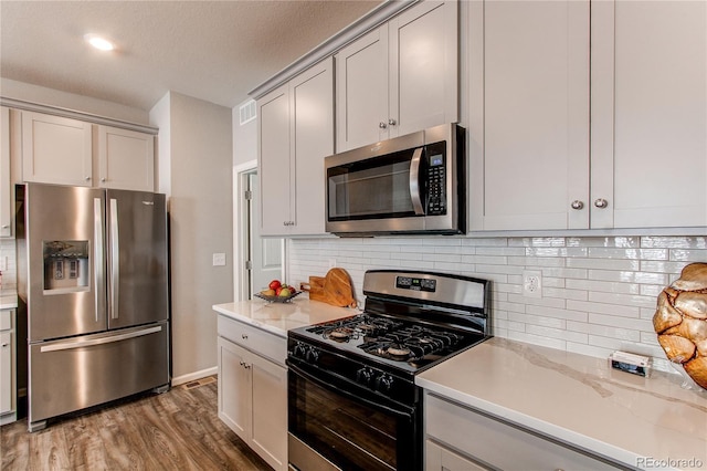 kitchen with stainless steel appliances, gray cabinetry, decorative backsplash, and wood finished floors
