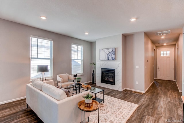 living room featuring dark wood-style flooring, baseboards, visible vents, and a fireplace