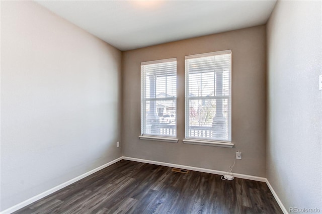 unfurnished room featuring baseboards, dark wood-style floors, and a wealth of natural light