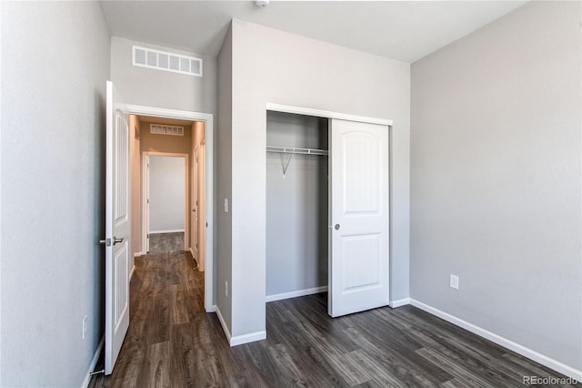 unfurnished bedroom with a closet, baseboards, visible vents, and dark wood-type flooring