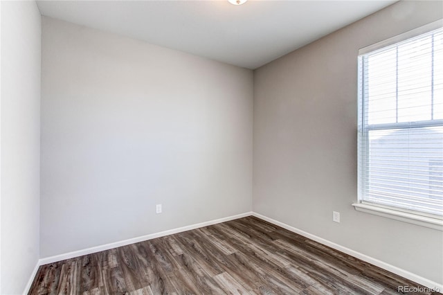 spare room with baseboards and dark wood-type flooring