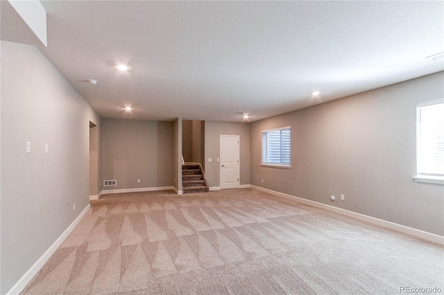 basement featuring visible vents, stairs, baseboards, and light carpet