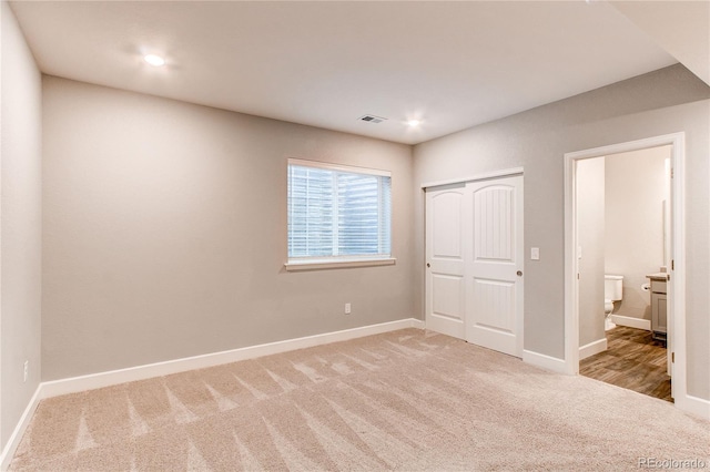unfurnished bedroom featuring visible vents, baseboards, a closet, connected bathroom, and light carpet