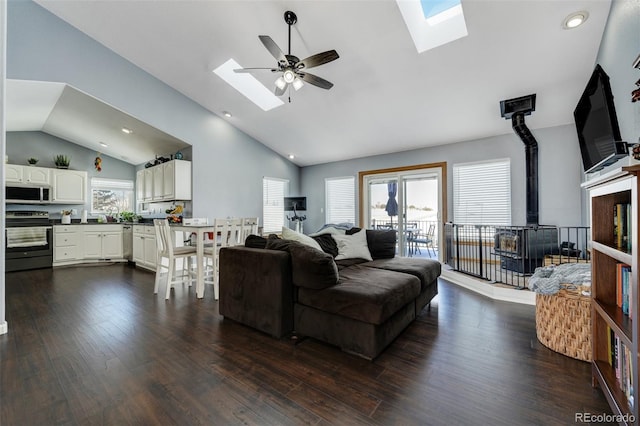 living room featuring dark hardwood / wood-style floors, high vaulted ceiling, a skylight, a wood stove, and ceiling fan