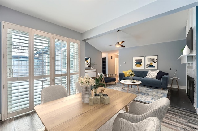 dining room with a fireplace, wood finished floors, a ceiling fan, baseboards, and vaulted ceiling