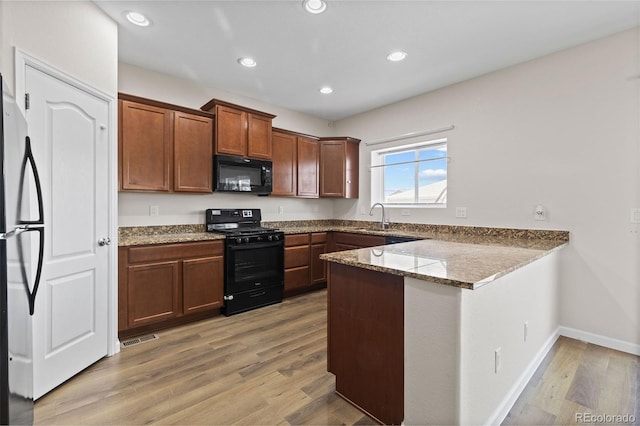 kitchen with sink, light hardwood / wood-style flooring, black appliances, stone countertops, and kitchen peninsula