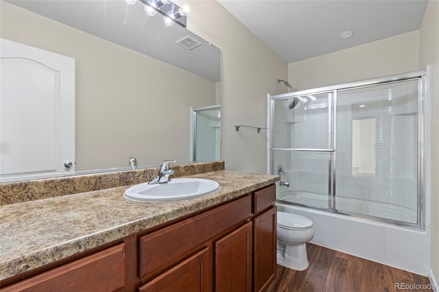 full bathroom featuring vanity, hardwood / wood-style flooring, shower / bath combination with glass door, and toilet