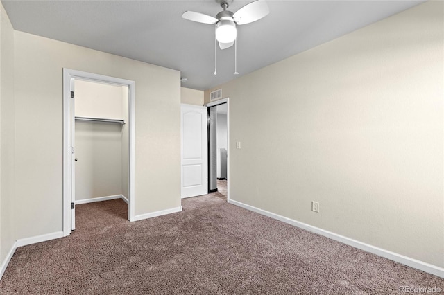 unfurnished bedroom featuring a spacious closet, a closet, ceiling fan, and dark colored carpet