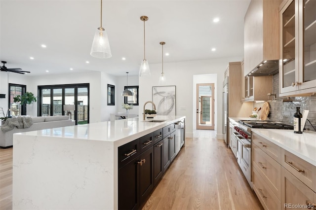 kitchen with pendant lighting, a spacious island, sink, wall chimney exhaust hood, and light hardwood / wood-style floors