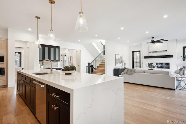 kitchen with sink, stainless steel appliances, hanging light fixtures, light hardwood / wood-style floors, and a center island with sink