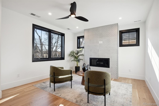 living area with ceiling fan, a large fireplace, and light hardwood / wood-style floors