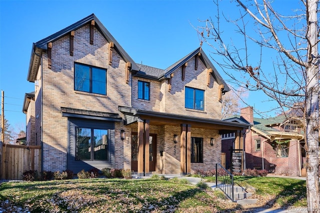 craftsman-style home with a front yard, brick siding, covered porch, and fence