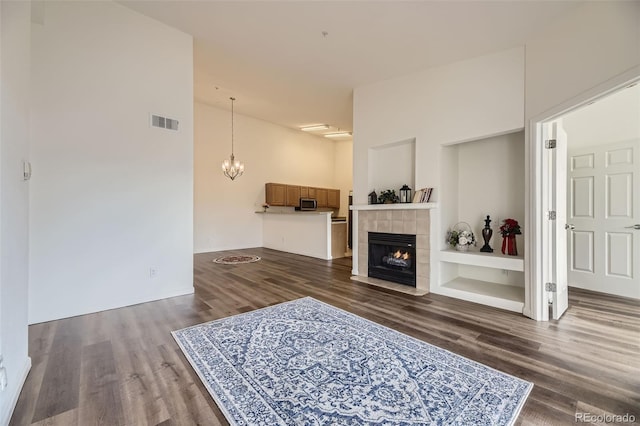 living room featuring a tile fireplace, a notable chandelier, a high ceiling, visible vents, and dark wood finished floors