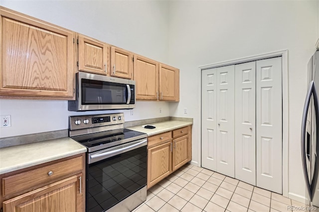 kitchen featuring light tile patterned floors, stainless steel appliances, light countertops, and a towering ceiling