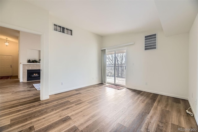 unfurnished living room with a tile fireplace, wood finished floors, visible vents, and baseboards