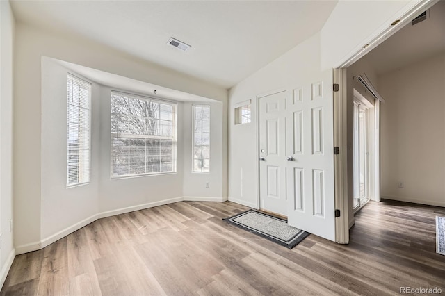 entrance foyer featuring visible vents, vaulted ceiling, baseboards, and wood finished floors