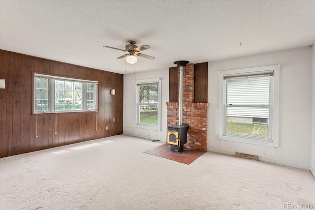 8005 W US Highway 50, Salida, CO 81201 - unfurnished living room featuring carpet flooring, a wood stove, a textured ceiling, wood walls, and ceiling fan