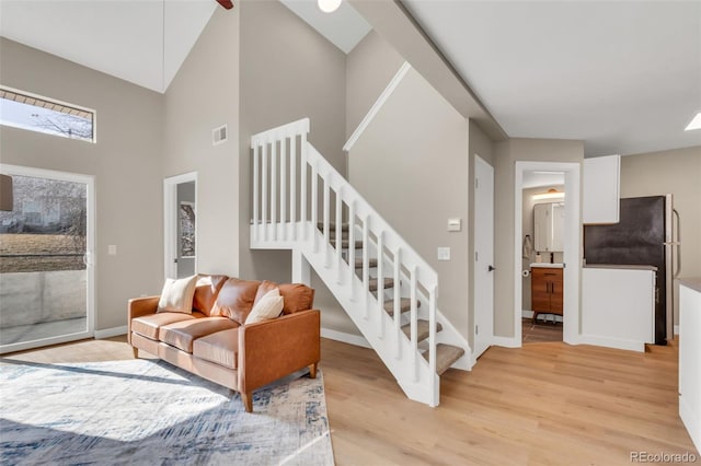 living area featuring a towering ceiling, visible vents, baseboards, light wood-style flooring, and stairs