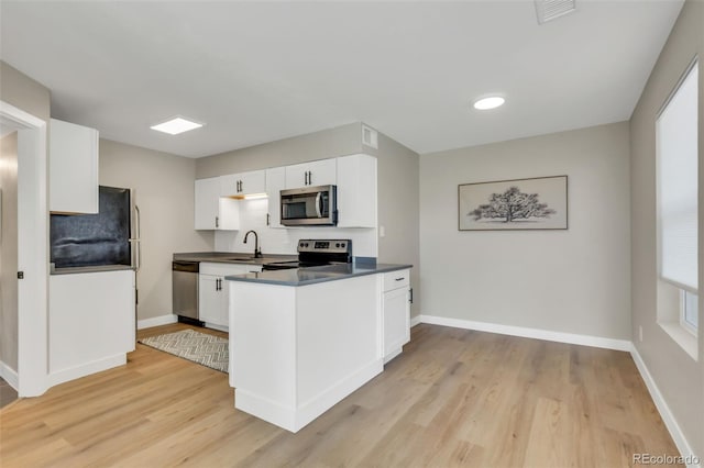 kitchen with white cabinets, stainless steel appliances, light wood finished floors, and dark countertops