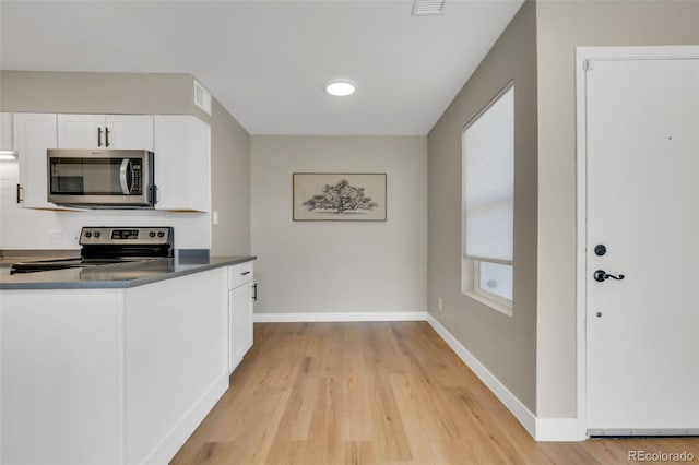 kitchen featuring light wood finished floors, stainless steel appliances, baseboards, and white cabinets
