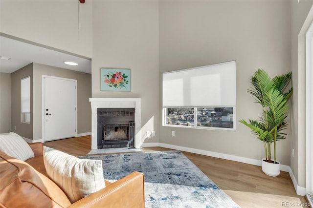 living room featuring a fireplace with flush hearth, baseboards, wood finished floors, and a high ceiling