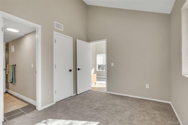 unfurnished bedroom with a towering ceiling, baseboards, visible vents, and carpet floors