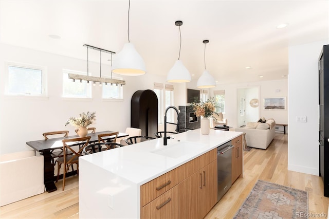 kitchen featuring pendant lighting, sink, a center island with sink, stainless steel dishwasher, and light wood-type flooring