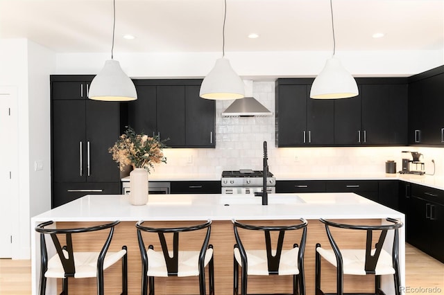 kitchen featuring wall chimney exhaust hood, an island with sink, and hanging light fixtures