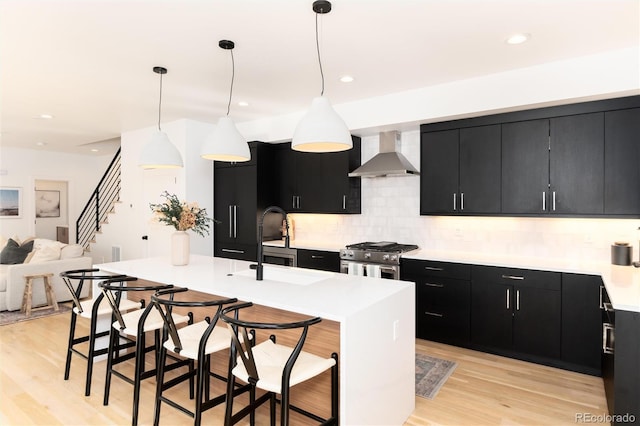 kitchen with wall chimney exhaust hood, a breakfast bar, decorative light fixtures, stainless steel stove, and an island with sink