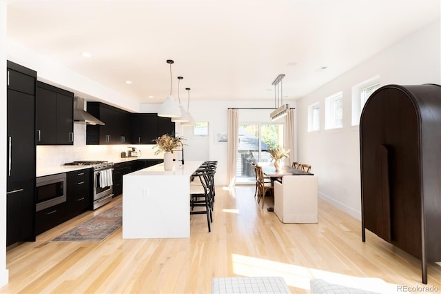 kitchen featuring wall chimney exhaust hood, a breakfast bar, decorative light fixtures, stainless steel appliances, and a kitchen island with sink