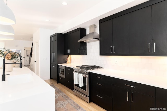 kitchen featuring decorative light fixtures, decorative backsplash, light hardwood / wood-style floors, stainless steel appliances, and wall chimney range hood