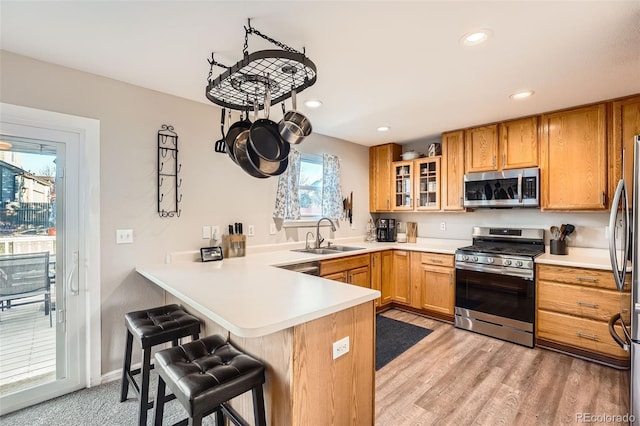 kitchen with kitchen peninsula, stainless steel appliances, sink, light hardwood / wood-style floors, and a breakfast bar area