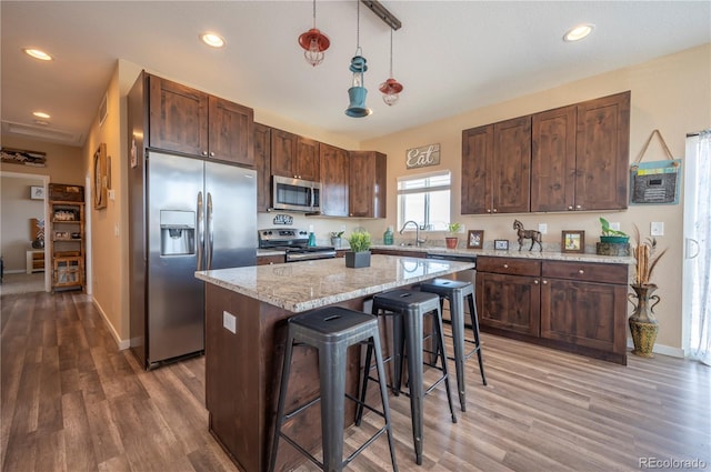kitchen with a kitchen island, appliances with stainless steel finishes, a breakfast bar, and light wood-type flooring