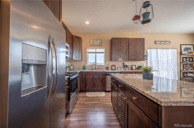 kitchen featuring dark wood-style floors, a sink, a kitchen island, light stone countertops, and appliances with stainless steel finishes