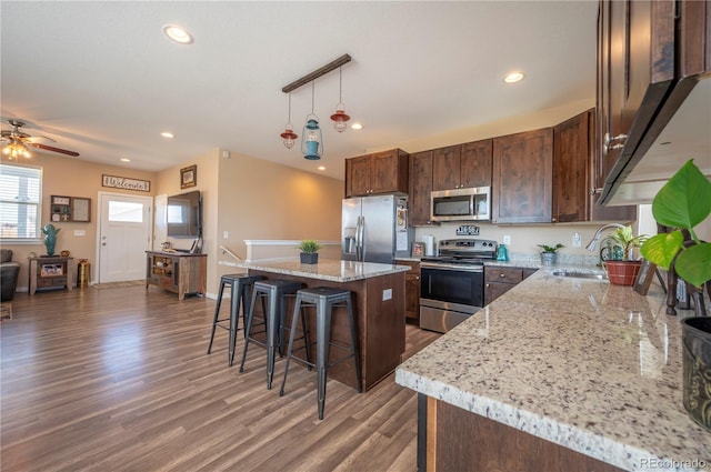 kitchen featuring a kitchen breakfast bar, wood finished floors, a sink, appliances with stainless steel finishes, and a kitchen island