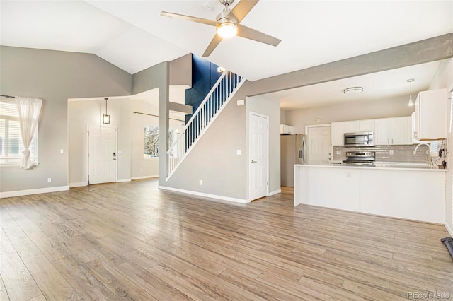 unfurnished living room with sink, light hardwood / wood-style flooring, ceiling fan, and vaulted ceiling