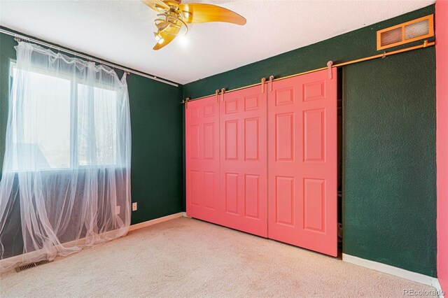 unfurnished bedroom with ceiling fan, a barn door, carpet floors, and a closet