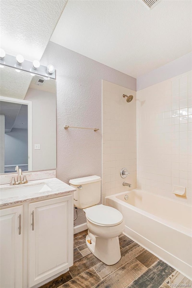 full bathroom featuring tiled shower / bath, vanity, toilet, and a textured ceiling