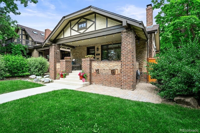 1414 S Vine St, Denver, CO 80210 - tudor house featuring a chimney, covered porch, a front yard, and brick siding