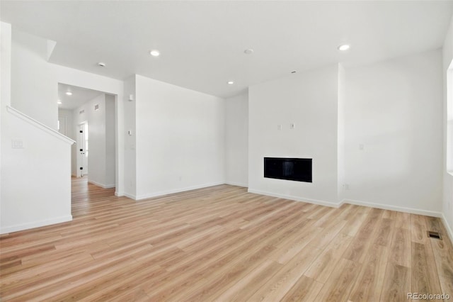 unfurnished living room featuring recessed lighting, a glass covered fireplace, light wood-style flooring, and baseboards