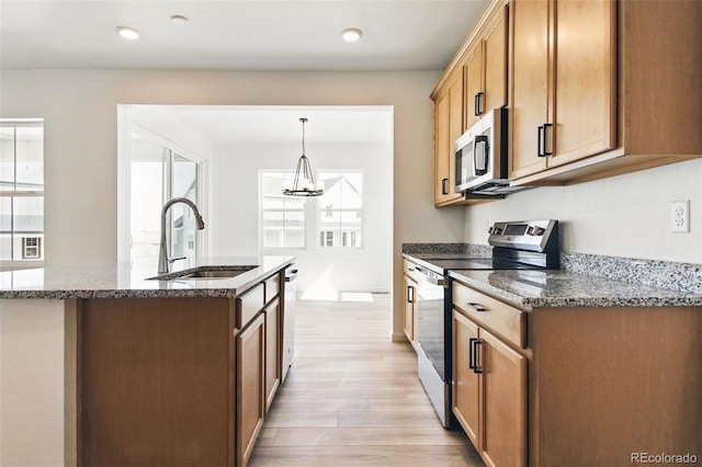 kitchen with a sink, dark stone countertops, light wood-type flooring, and stainless steel appliances