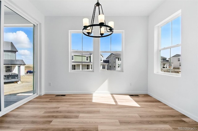 unfurnished dining area featuring a notable chandelier, visible vents, baseboards, and wood finished floors