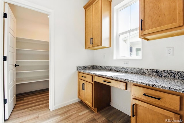 kitchen featuring light stone countertops, built in desk, light wood finished floors, and baseboards