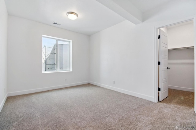 unfurnished bedroom with carpet, baseboards, visible vents, beam ceiling, and a walk in closet