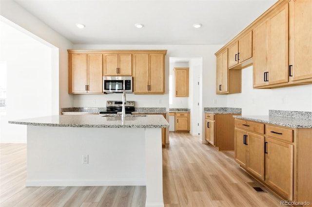 kitchen featuring visible vents, an island with sink, light stone counters, stainless steel appliances, and light wood finished floors