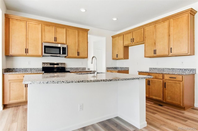 kitchen with light stone counters, light wood-style flooring, an island with sink, a sink, and stainless steel appliances