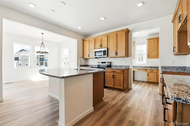 kitchen with stainless steel appliances, light wood-type flooring, dark stone counters, and a sink